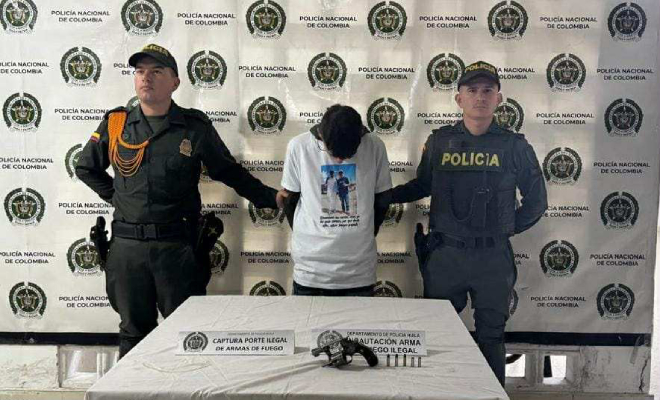 Dos policias con un hombre capturado en el medio, y un arma de fuego en una mesa