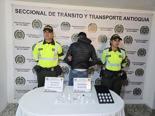Dos policías de transito y transportes custodian a un capturado y esmeraldas incautadas