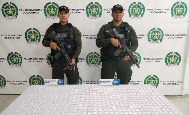 Hombre capturado en medio de dos policías, en frente estuperfacientes incautados