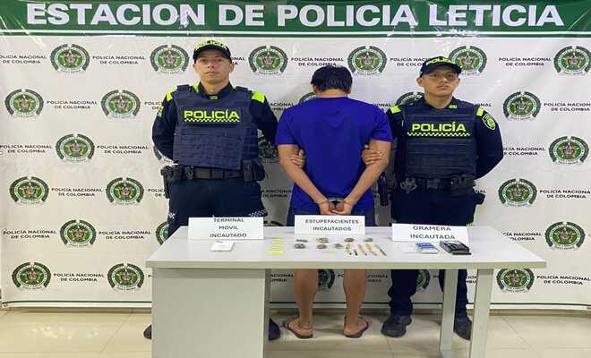 Dos policías, una persona capturada de espaldas y encima de una mesa elementos incautados