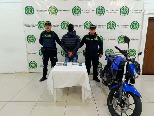 hombre capturado de espalda en medio de dos Policias, en frente se encuentra la motocicleta recuperada