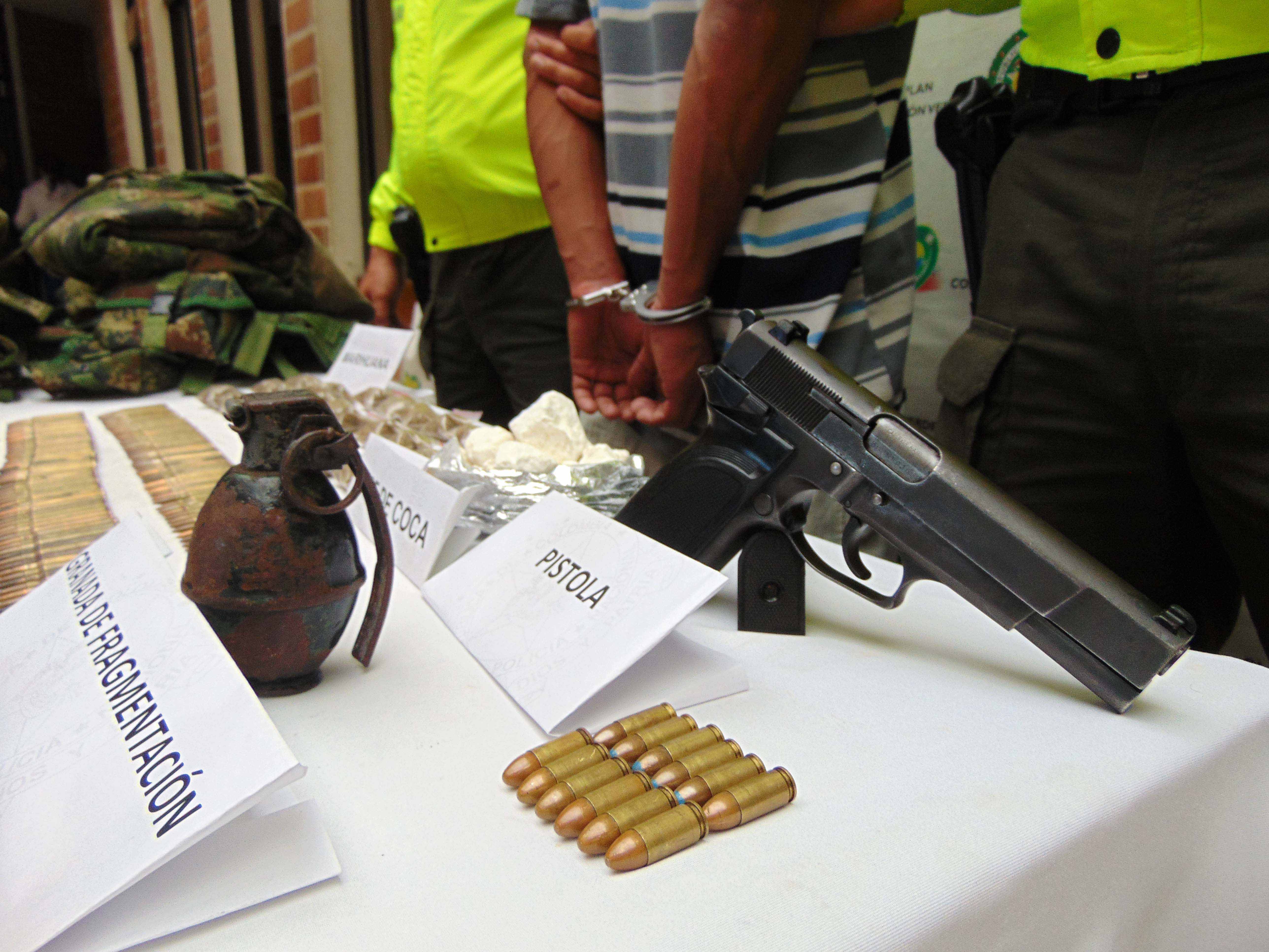 Hombre capturado con arma, granada, munición y droga es custodiado por dos policías de la Sijin en Medellín