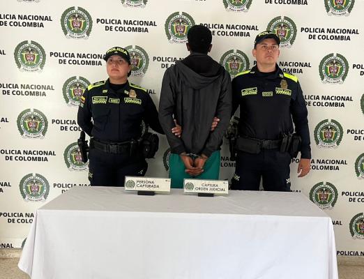 Hombre capturado de espalda con chaqueta negra en medio de dos Policias
